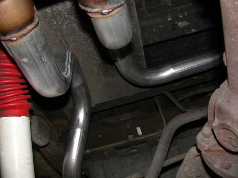 1996 Ford Bronco - Underside view of new stainless steel exhaust pipes routed downward from the catalytic converters/mufflers, with a red-and-white coilover s…