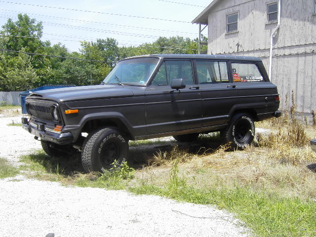 Dark gray 1977 Jeep Wagoneer parked on gravel with dry grass, side view