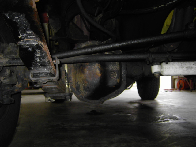 Underside view of a solid front axle with differential, leaf spring and white steering stabilizer