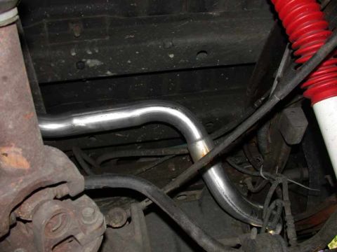 1996 Ford Bronco - An underbody shot of a newly installed polished stainless exhaust pipe routed with a jog over the frame rail and axle area of a truck. A re…