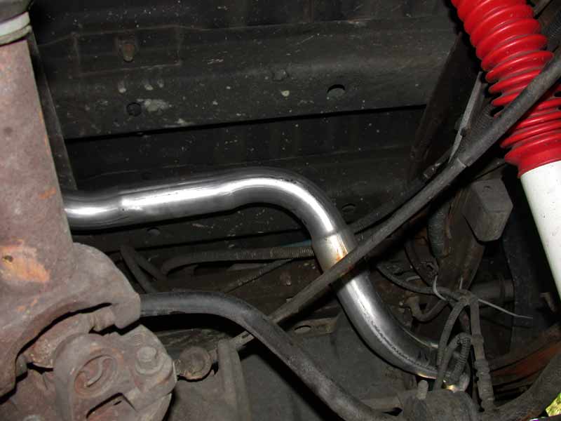 Polished stainless exhaust pipe routed under a truck chassis next to a red-boot shock