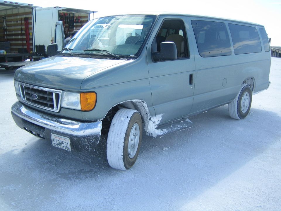 gray Ford Econoline van with salt-caked wheels parked on a white flat