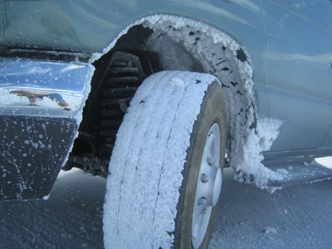 1990 Ford Bronco - Close-up of a van's front wheel and fender heavily caked with white salt and slush.