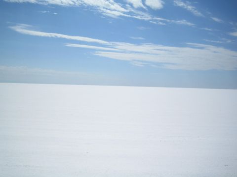 1990 Ford Bronco - featureless bright white salt flat extends to the horizon under a blue sky with thin streaky clouds.