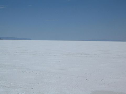 1990 Ford Bronco - wide white salt flat marked with faint tracks stretches to distant hills under a clear blue sky.