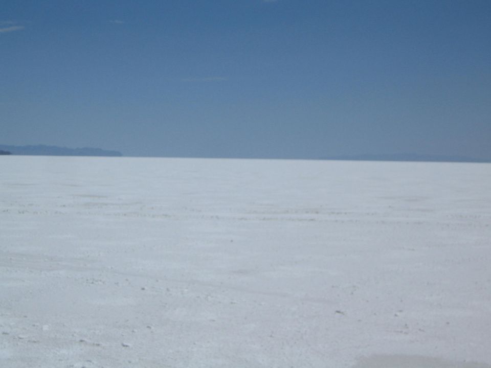 wide white salt flat with faint tracks under a clear blue sky
