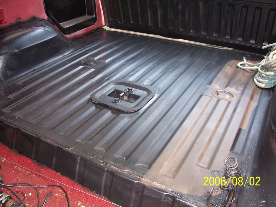 Black painted ribbed rear cargo floor of a Bronco with center access panel and coiled rope