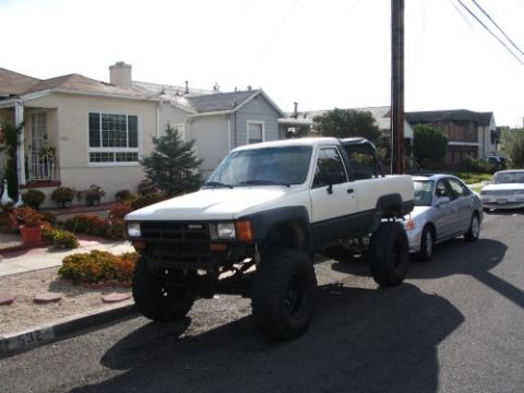 1985 Toyota 4Runner - A modified pickup truck with oversized tires is parked on a residential street next to another car.