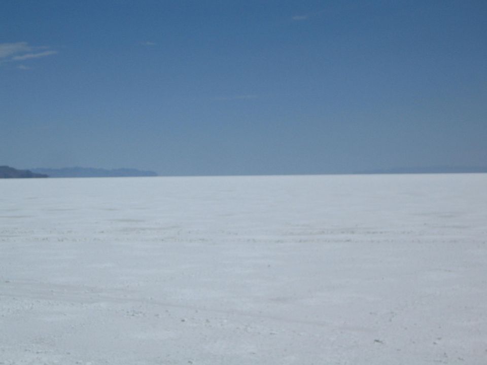 broad white salt flat meeting distant mountains under a blue sky