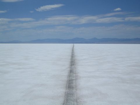 1990 Ford Bronco - dark vehicle track runs straight across a white salt flat toward distant mountains under a blue sky.