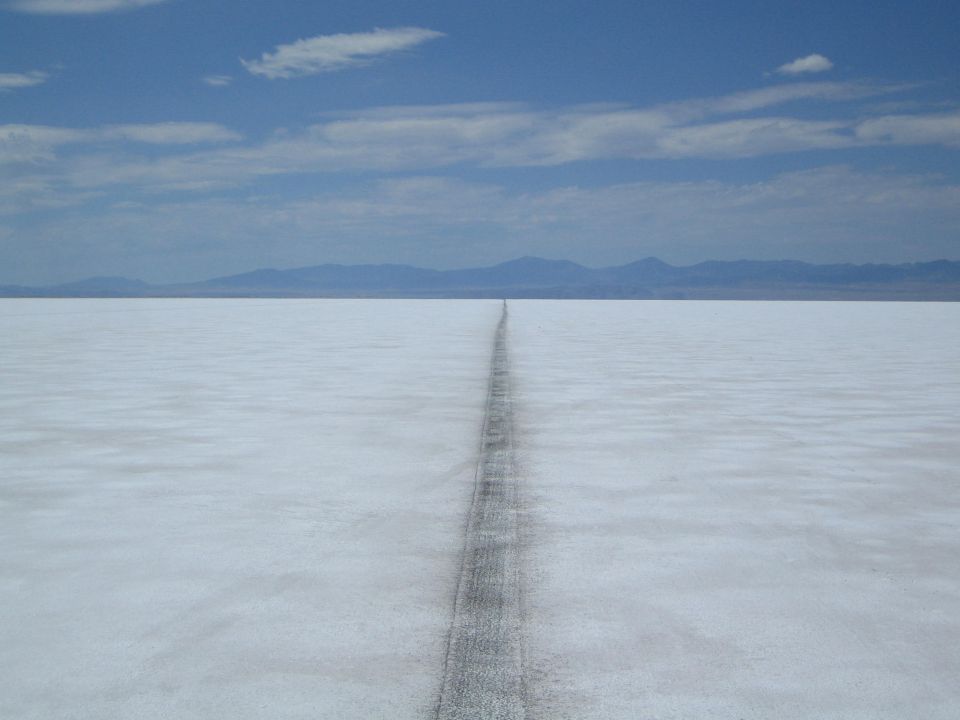 dark track running straight across a white salt flat toward mountains