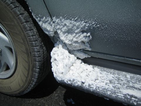 1990 Ford Bronco - Thick white salt residue cakes the rocker panel and sidewall area behind a vehicle's front tire.