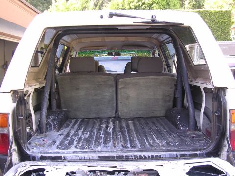 1985 Toyota 4Runner - The interior of an SUV shows a folded rear seat and an empty cargo bed with a roll cage structure.