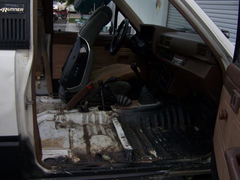 1985 Toyota 4Runner - The interior of a 1985 Toyota 4Runner shows a worn driver's seat and a dirty floor, with the 'Toyota 4Runner' badge visible on the door pan…