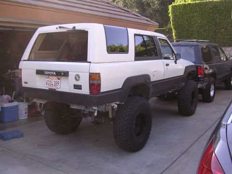 1985 Toyota 4Runner - A modified white Toyota 4Runner is parked next to other vehicles, showing its lifted suspension and large off-road tires.