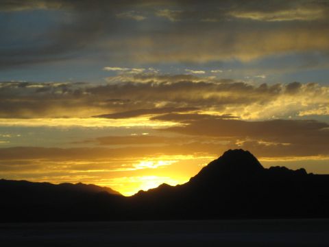 1990 Ford Bronco - sun sets in orange and gold tones behind a dark mountain range over a flat desert horizon.