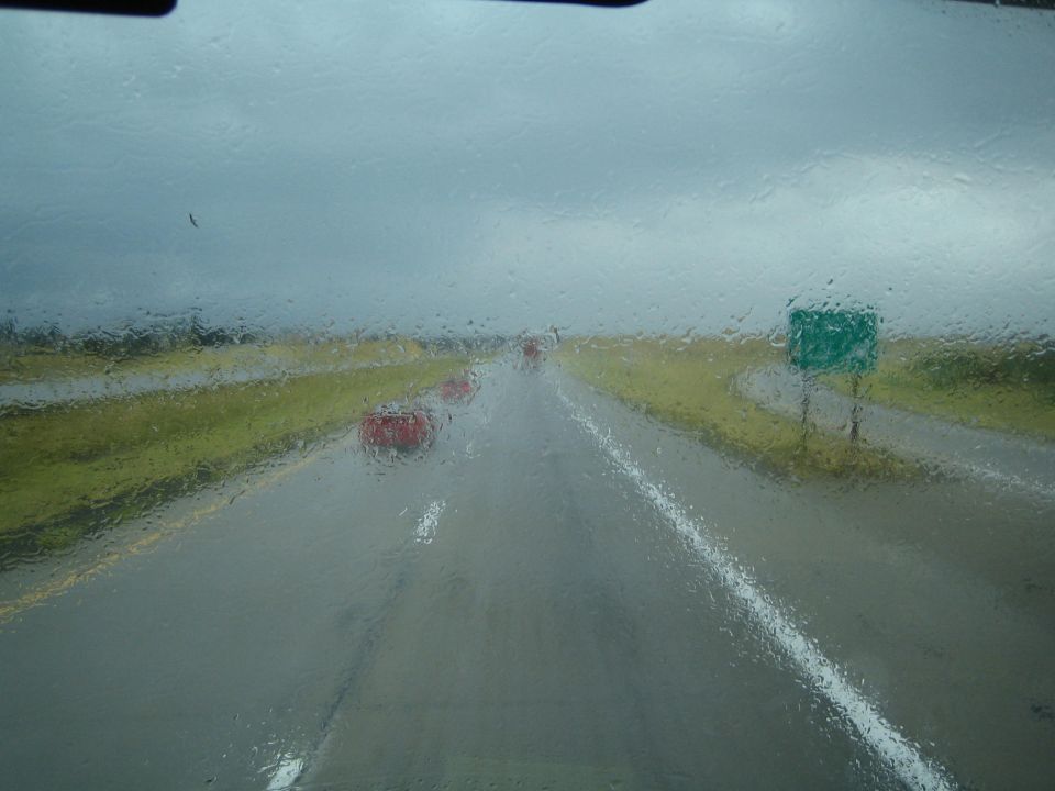 Rainy highway seen through a wet windshield with red and green signs