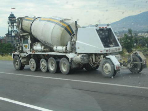 1990 Ford Bronco - white cement mixer truck travels along a highway with hills and a tower structure in the background.