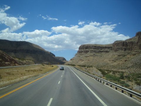1990 Ford Bronco - divided highway runs through a desert landscape of layered rocky mesas under a partly cloudy blue sky.