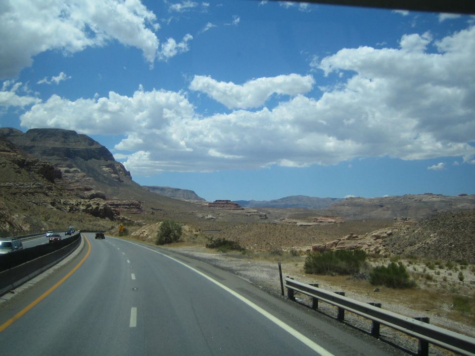 Desert highway descending into a valley with mesas and cars ahead
