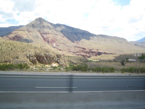 1990 Ford Bronco - layered red-and-tan rock mountain rises beyond a highway guardrail in a desert landscape.