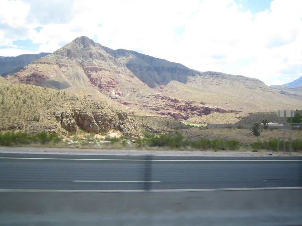 Layered red and tan mountain seen from a highway behind a guardrail