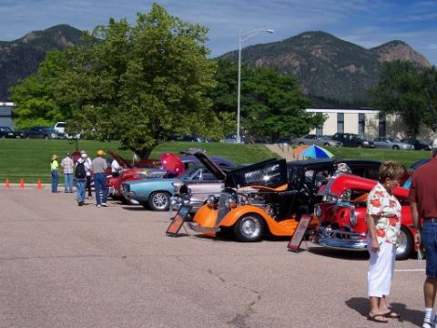 1972 Ford Ranchero - An orange hot rod is displayed with its hood open at a car show, with other vehicles and spectators present.