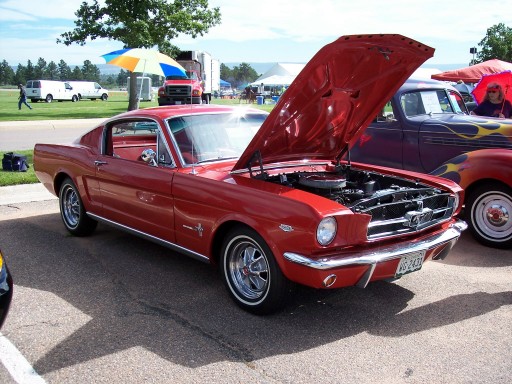Red 1960s Ford Mustang fastback with hood up at a car show