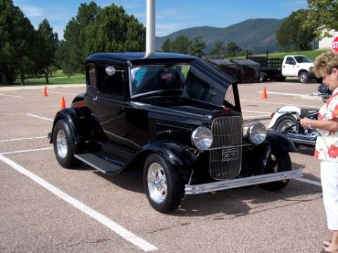 1972 Ford Ranchero - Black 1928 Ford Model A coupe hot rod with hood open, parked in a lot with mountains in background.