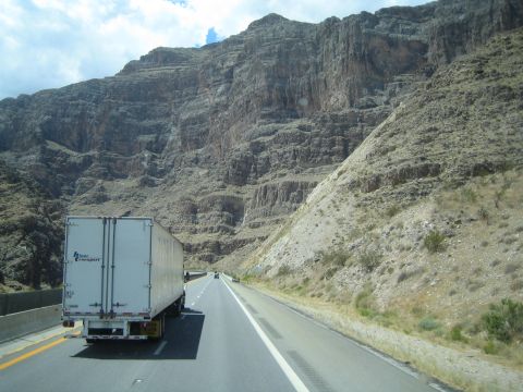 1990 Ford Bronco - white box semi-truck travels a highway running alongside tall striated rock cliffs in a canyon.