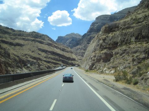 1990 Ford Bronco - highway winds through a steep rugged canyon with cars on the road and rocky mountain walls on both sides.