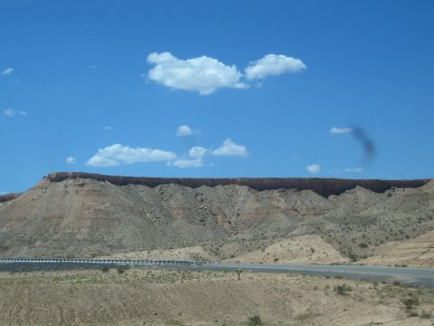 1990 Ford Bronco - long eroded desert ridge with a flat top stretches under a blue sky above a roadside guardrail.