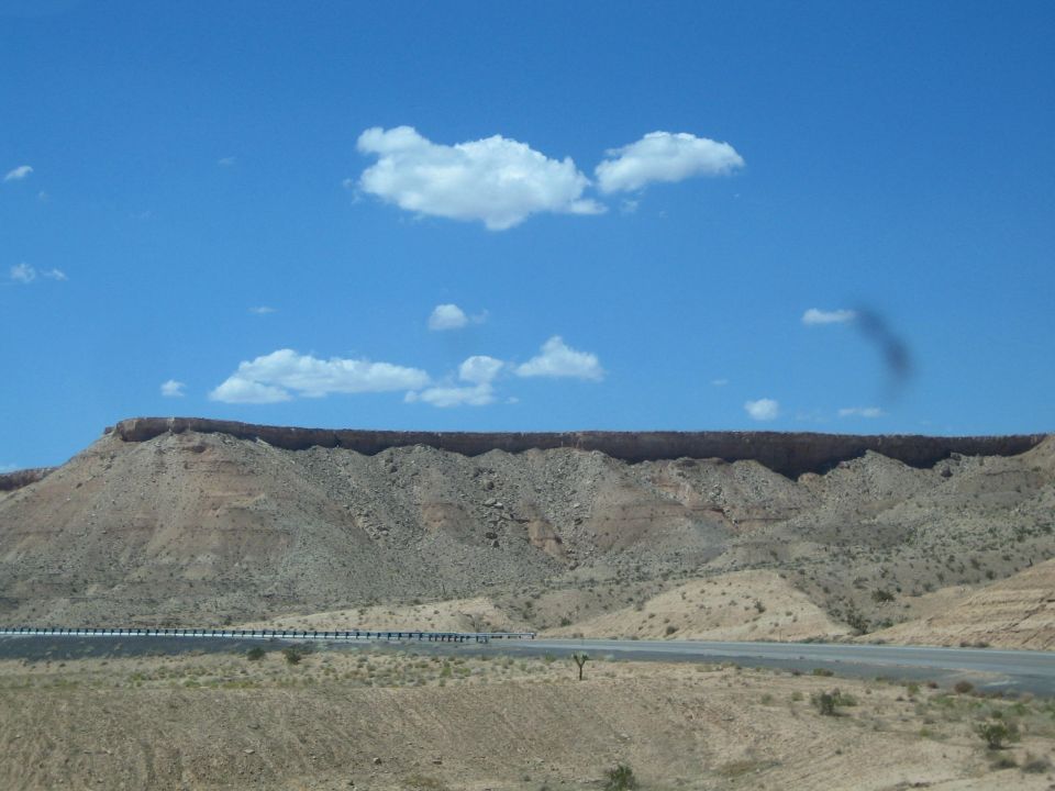 Long flat-topped desert mesa under a blue sky beside a highway