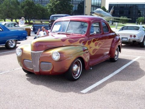 1972 Ford Ranchero - A custom hot rod with flame graphics is parked in a lot, with other vehicles and an airplane in the background.