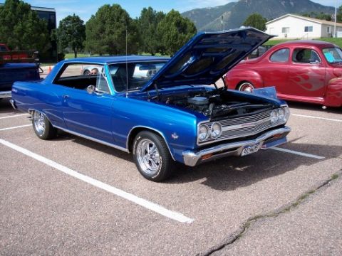1972 Ford Ranchero - A blue coupe is parked with its hood open, showing the engine bay. Another car is parked nearby.