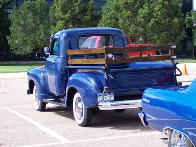 1972 Ford Ranchero - A blue 1950s Chevrolet pickup truck is parked next to another blue vehicle, with trees in the background.