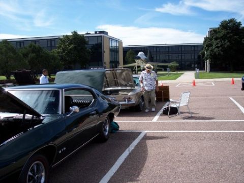 1972 Ford Ranchero - A dark green coupe, possibly a Pontiac GTO, is displayed with its hood open at an outdoor event alongside other vehicles and an airplane.