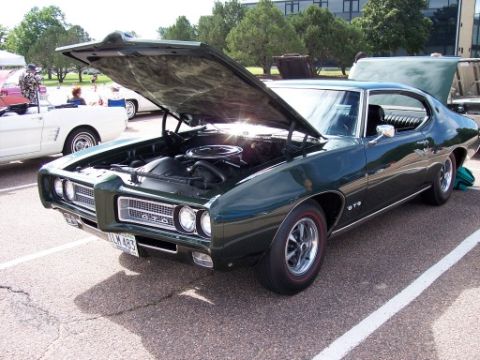 1972 Ford Ranchero - Dark green 1969 Pontiac GTO with hood open, parked next to a white car.