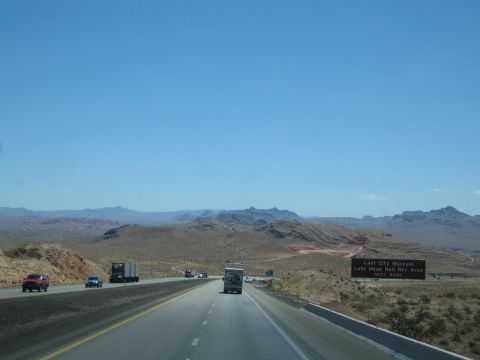 1990 Ford Bronco - Traffic moves along a desert highway past rocky hills, with a brown recreation-area sign on the right shoulder.