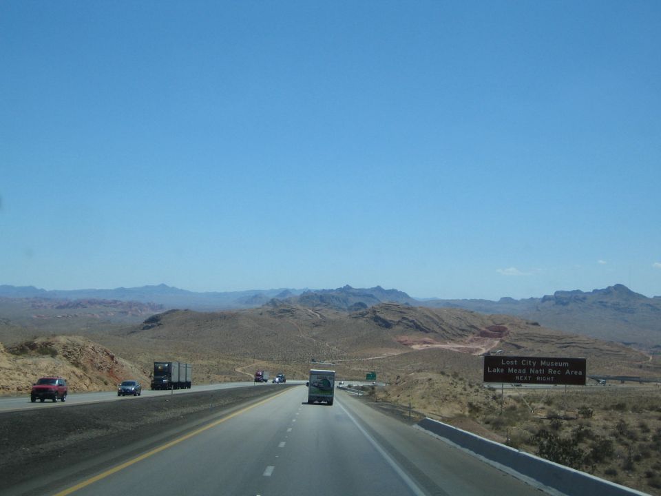 Desert highway with traffic and a brown park sign on the right