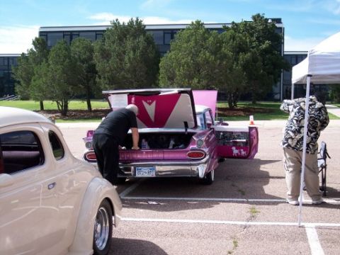 1972 Ford Ranchero - Two custom cars are parked outside a building, one with its trunk and door open.