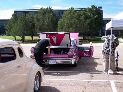 Pink 1959 Chevrolet with open trunk display at an outdoor car show, tan coupe alongside