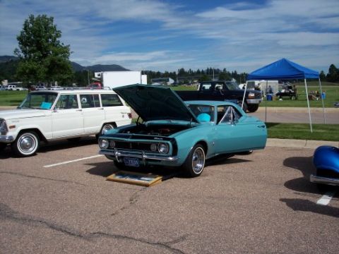 1972 Ford Ranchero - A teal coupe, possibly a 1967 model, is displayed with its hood open next to a white SUV and under a blue tent.