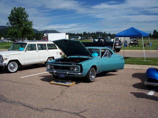 Turquoise 1960s two-door hardtop with hood up at an outdoor car show beside a white Jeep Wagoneer