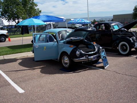 1972 Ford Ranchero - A light blue Volkswagen Beetle is displayed with its hood and door open, parked next to another vehicle at an outdoor event.