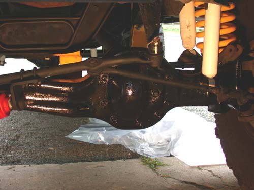 Freshly painted black solid front axle with orange coil springs seen from underneath