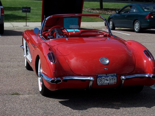 Red 1950s Chevrolet Corvette convertible with trunk open, rear three-quarter view at a car show