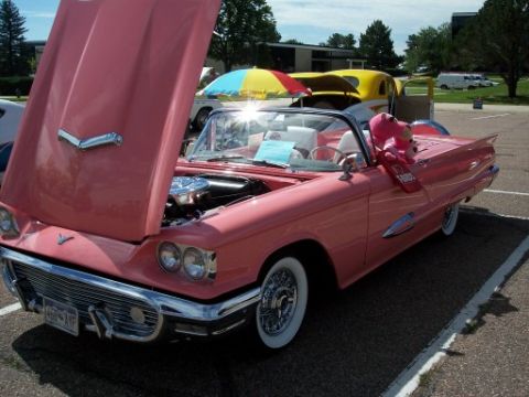 1972 Ford Ranchero - A pink 1958 Ford Thunderbird convertible is displayed with its hood up, revealing the engine, while other vehicles are visible in the backg…