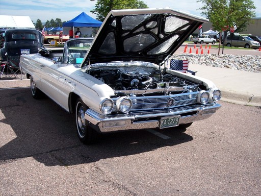 White early-1960s Buick convertible with hood open showing V8 engine at an outdoor car show