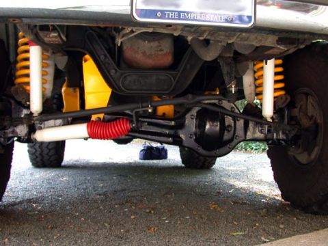 1996 Ford Bronco - View under the front of a lifted truck showing a solid front axle with black-painted differential, orange coil springs, white-bodied shocks…